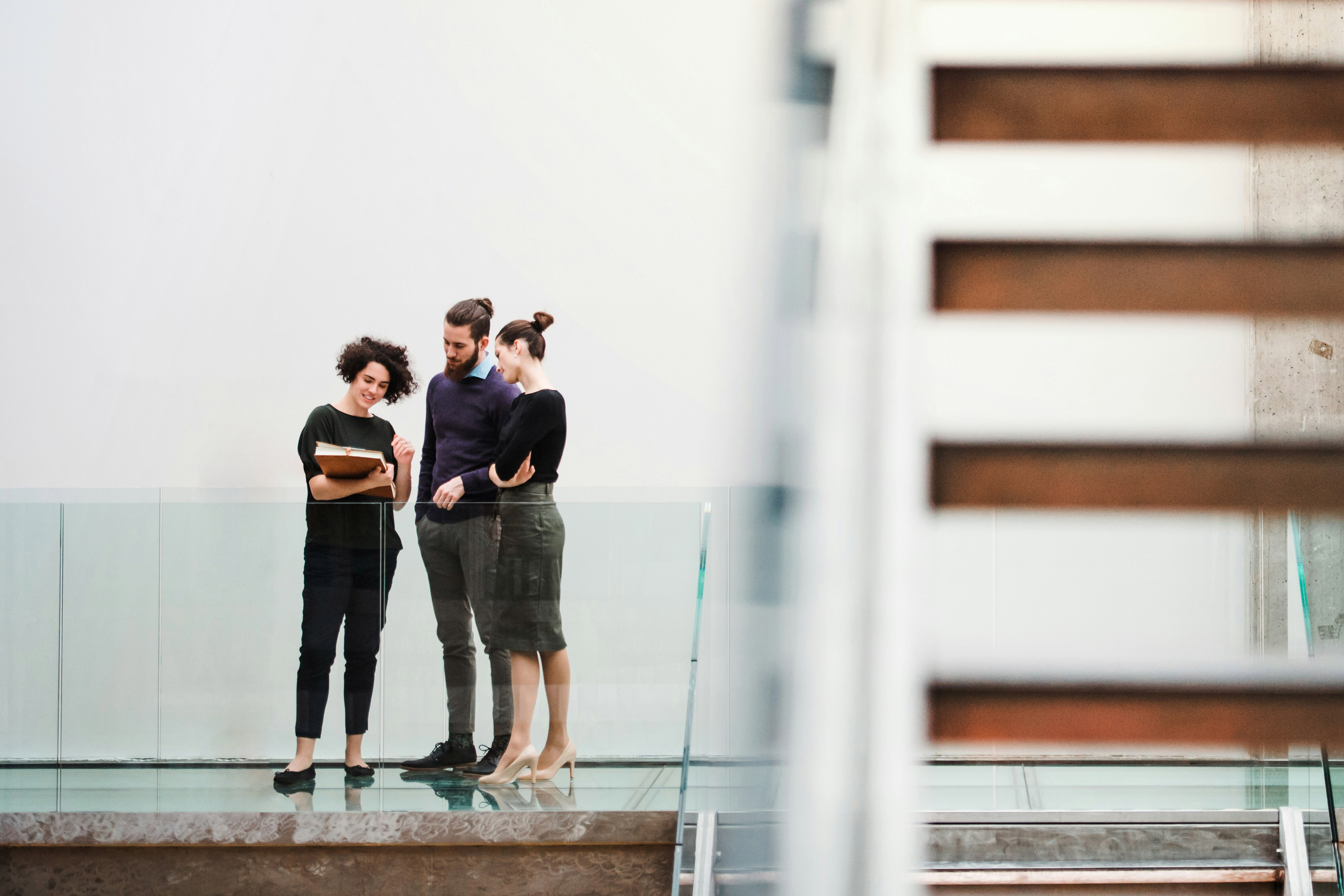 Three colleagues standing on glass floor reading a document together in a modern office.