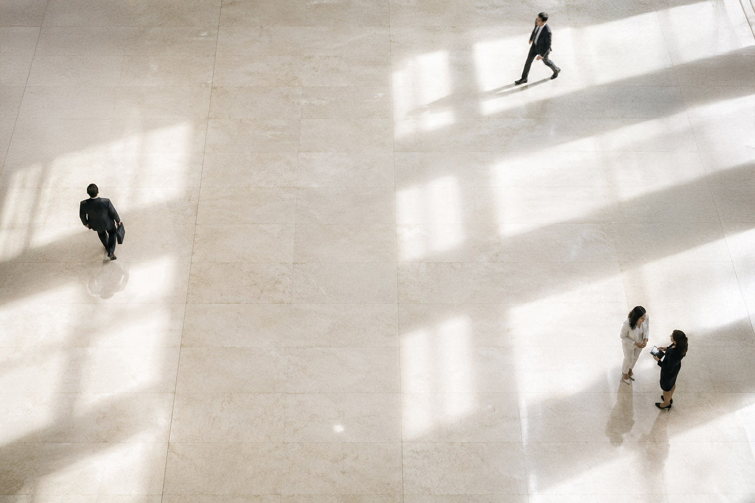 Overhead view of four business people in a bright open space with tiled floor and long shadows.