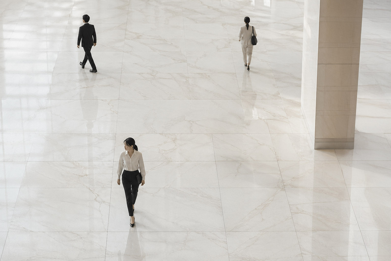 Three business people walking in a large, bright space with polished marble floors and a pillar.