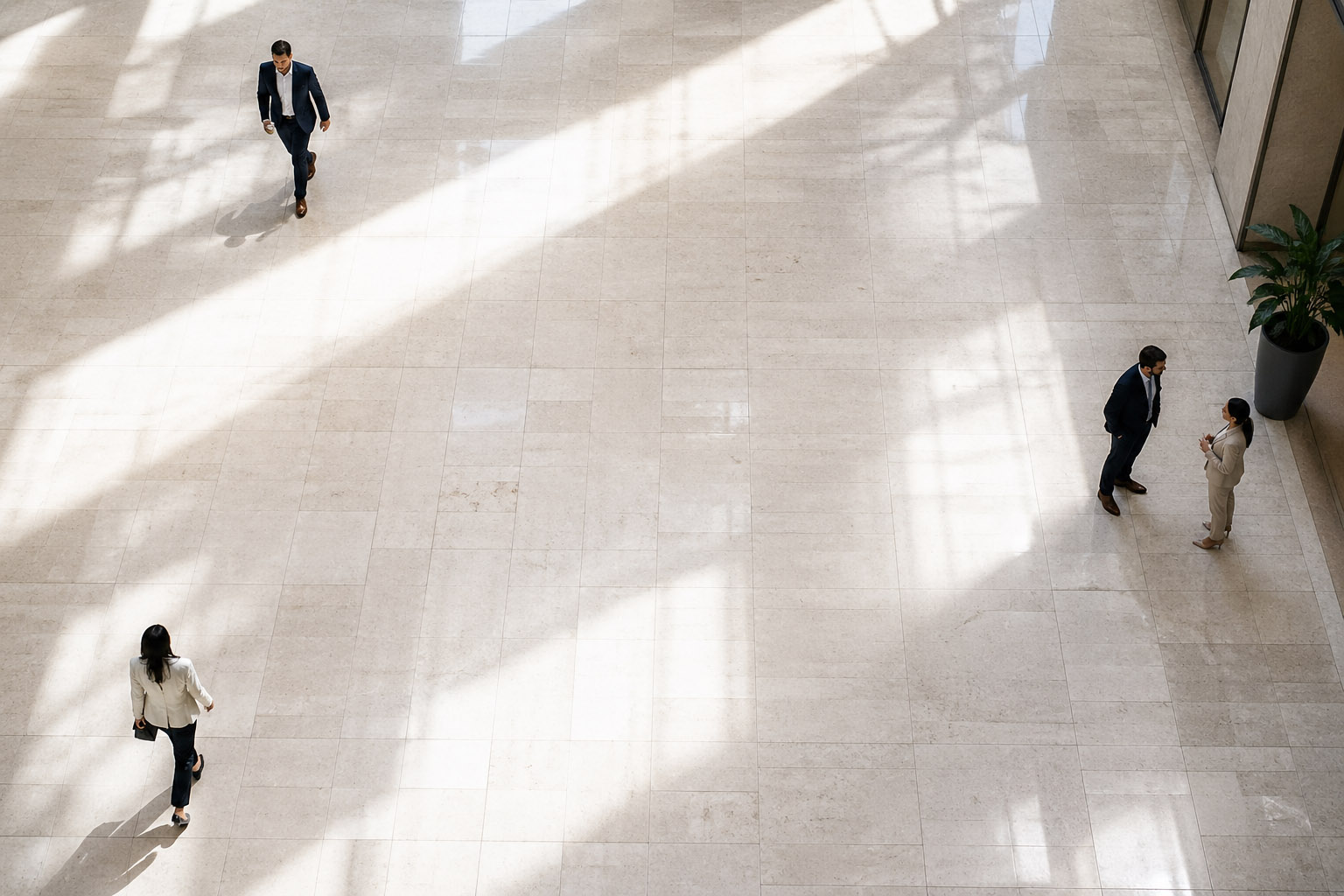 Four people in business attire in a spacious, sunlit lobby with marble flooring and a large plant.