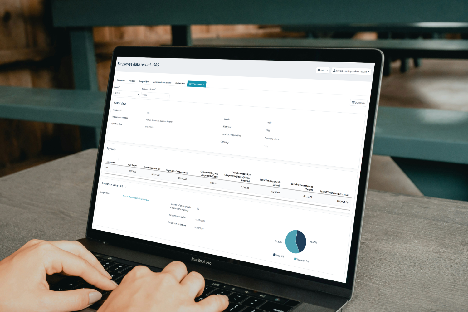 Laptop screen showing employee data record with pay transparency and compensation details for HR Business Partner.