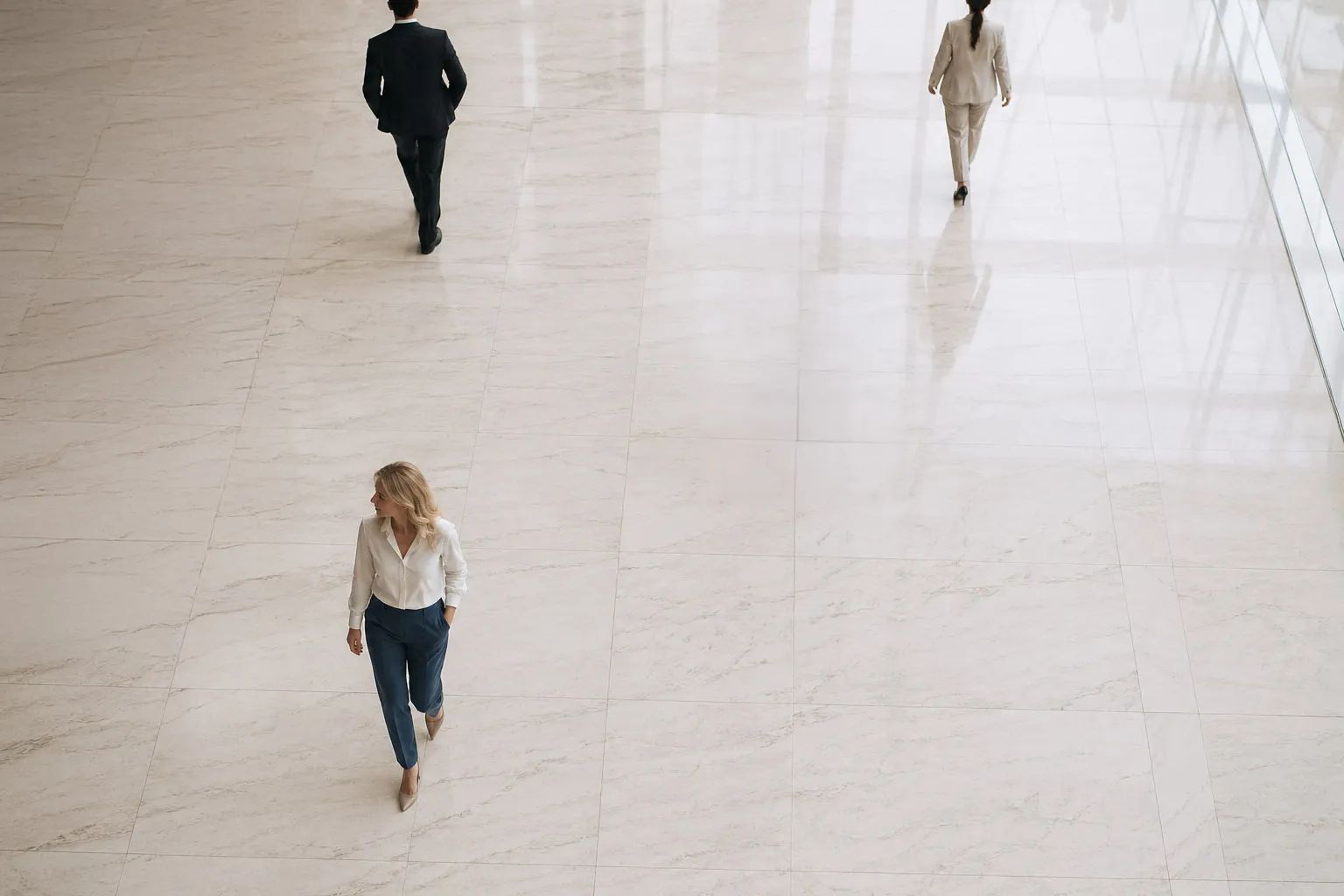 Trois hommes d'affaires marchent côte à côte sur un grand sol en marbre clair dans un immeuble de bureaux.