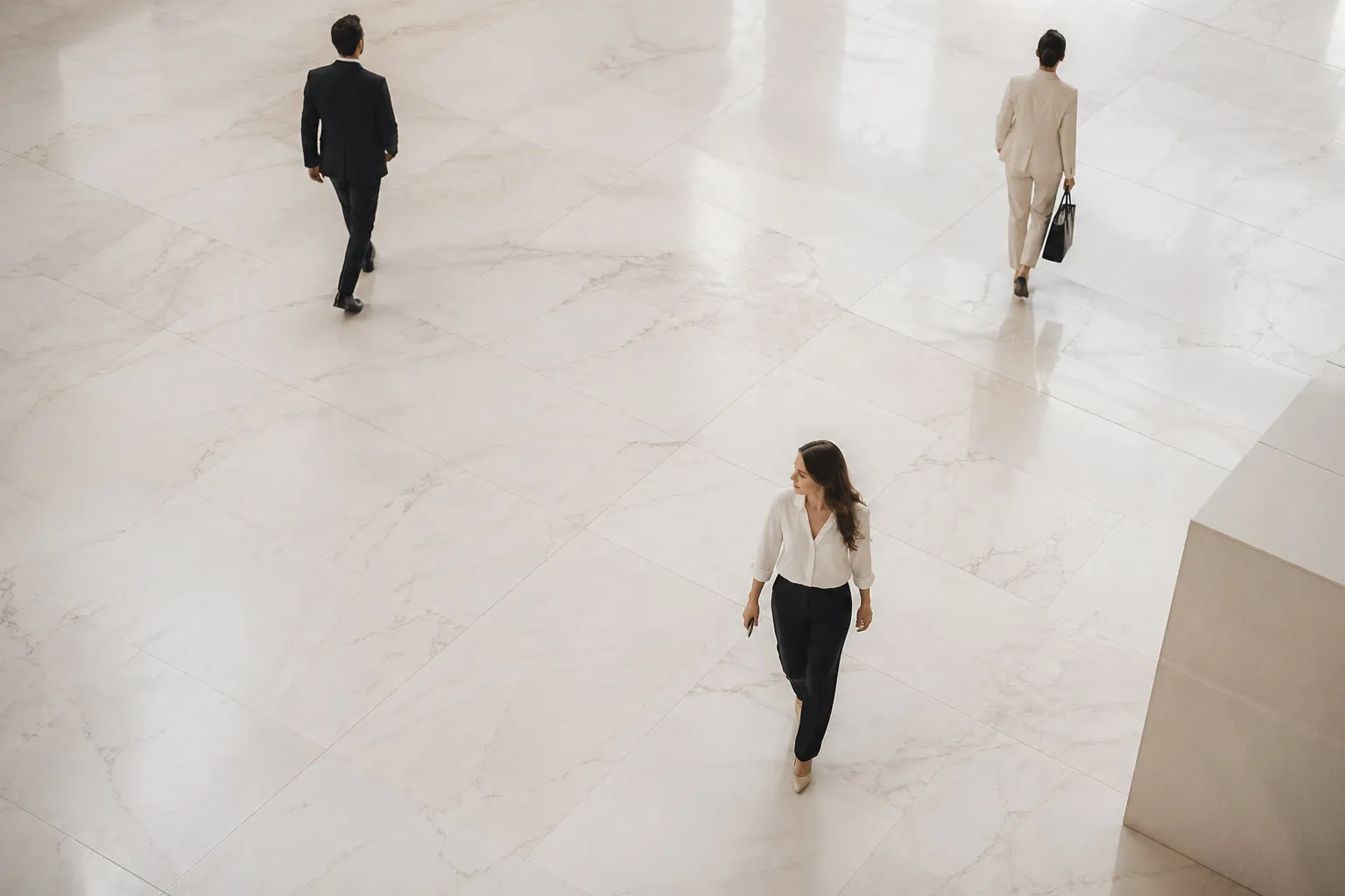 Three business people walking apart on a polished marble floor in an open indoor space.