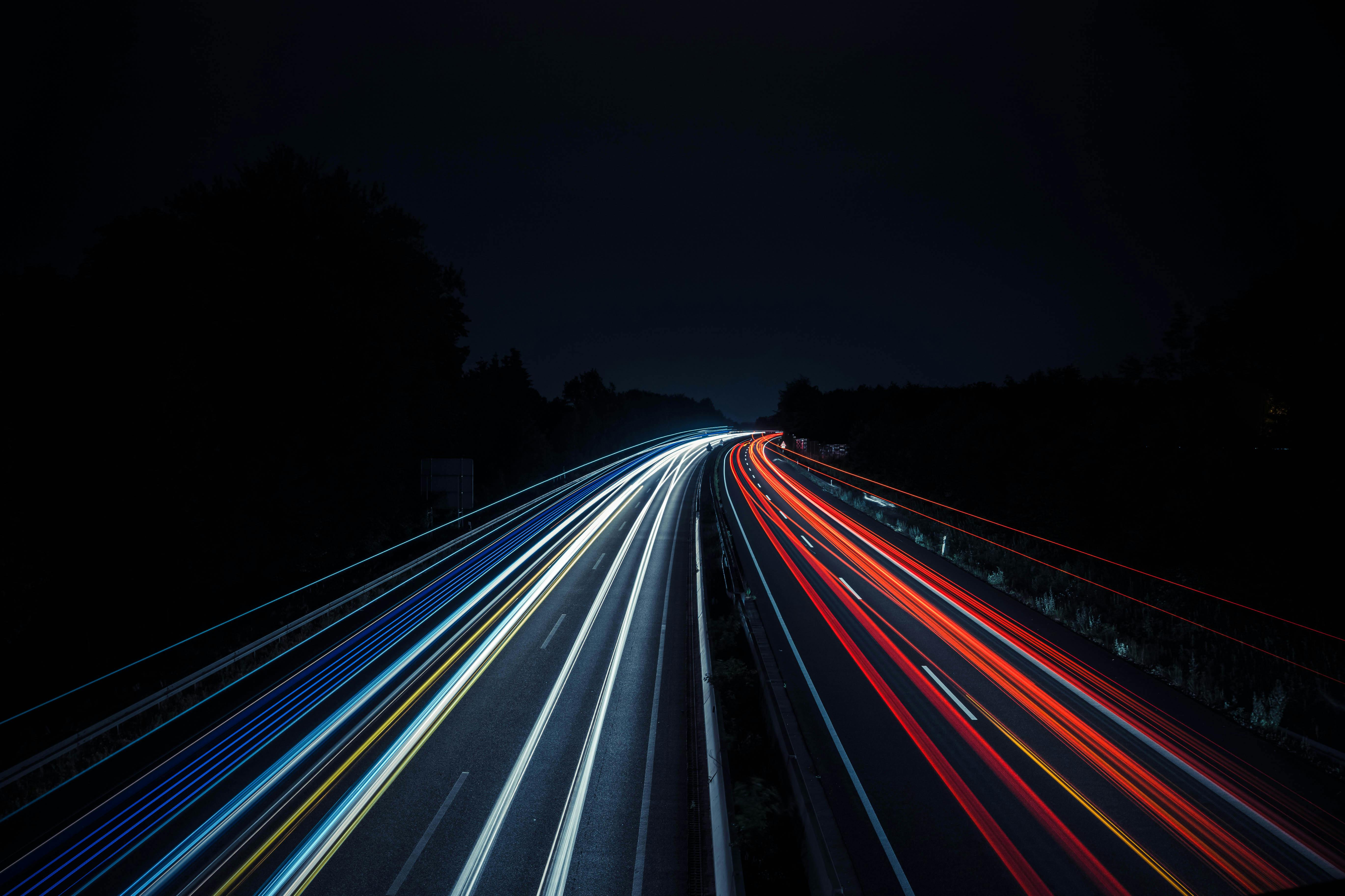 Long-exposure photo of a highway at night showing white and red light trails from moving vehicles.
