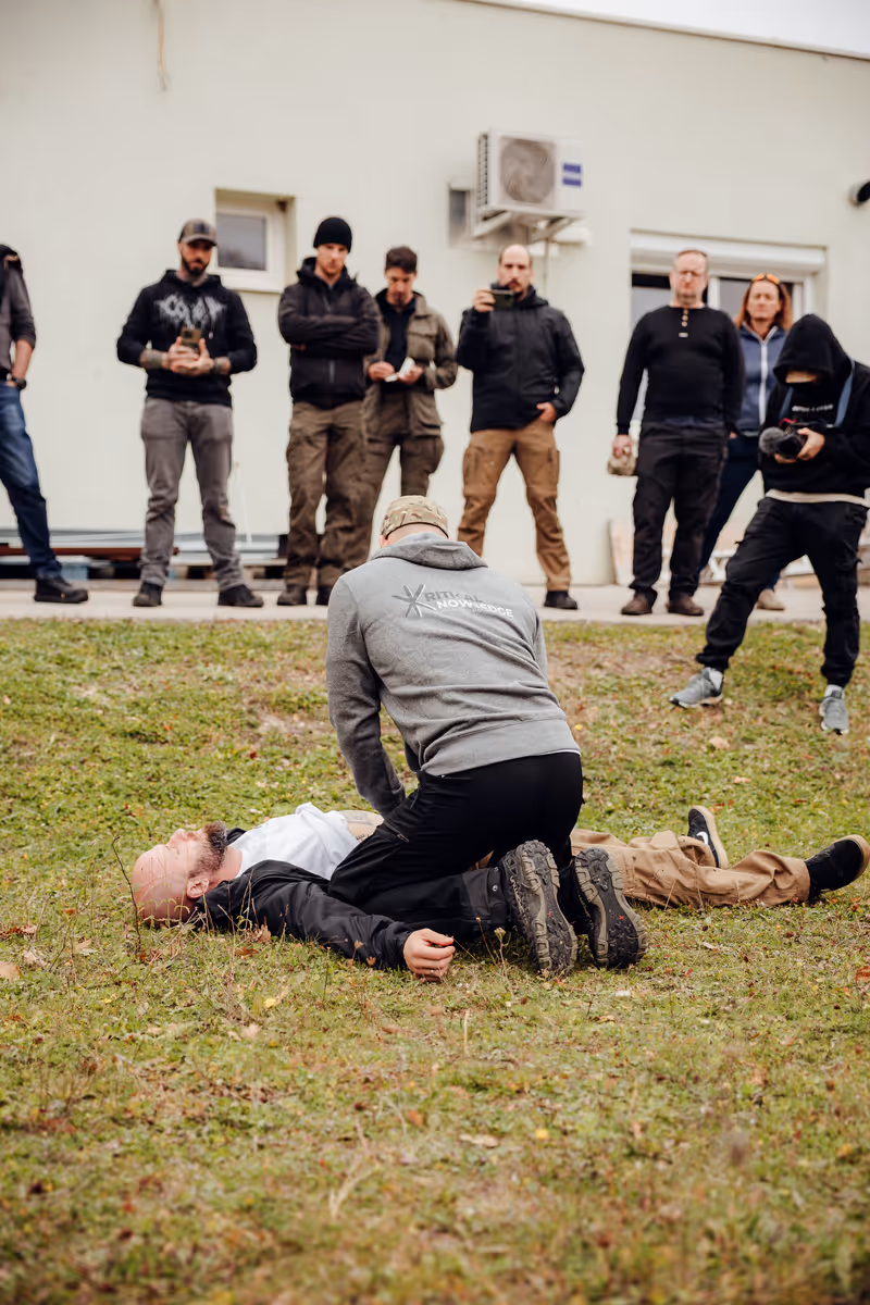 Erste-Hilfe-Training im Freien mit einer Person, die Herz-Lungen-Wiederbelebung an einer am Boden liegenden Person durchführt, während andere zuschauen.