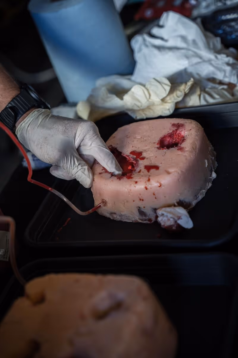 Hand mit Handschuh berührt eine blutige Wunde in einer realistischen Erste-Hilfe-Trainingsattrappe.