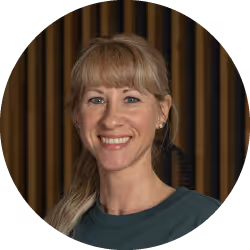 Frau mit blondem Haar, die lächelt vor einem Hintergrund mit vertikalen braunen und schwarzen Streifen.