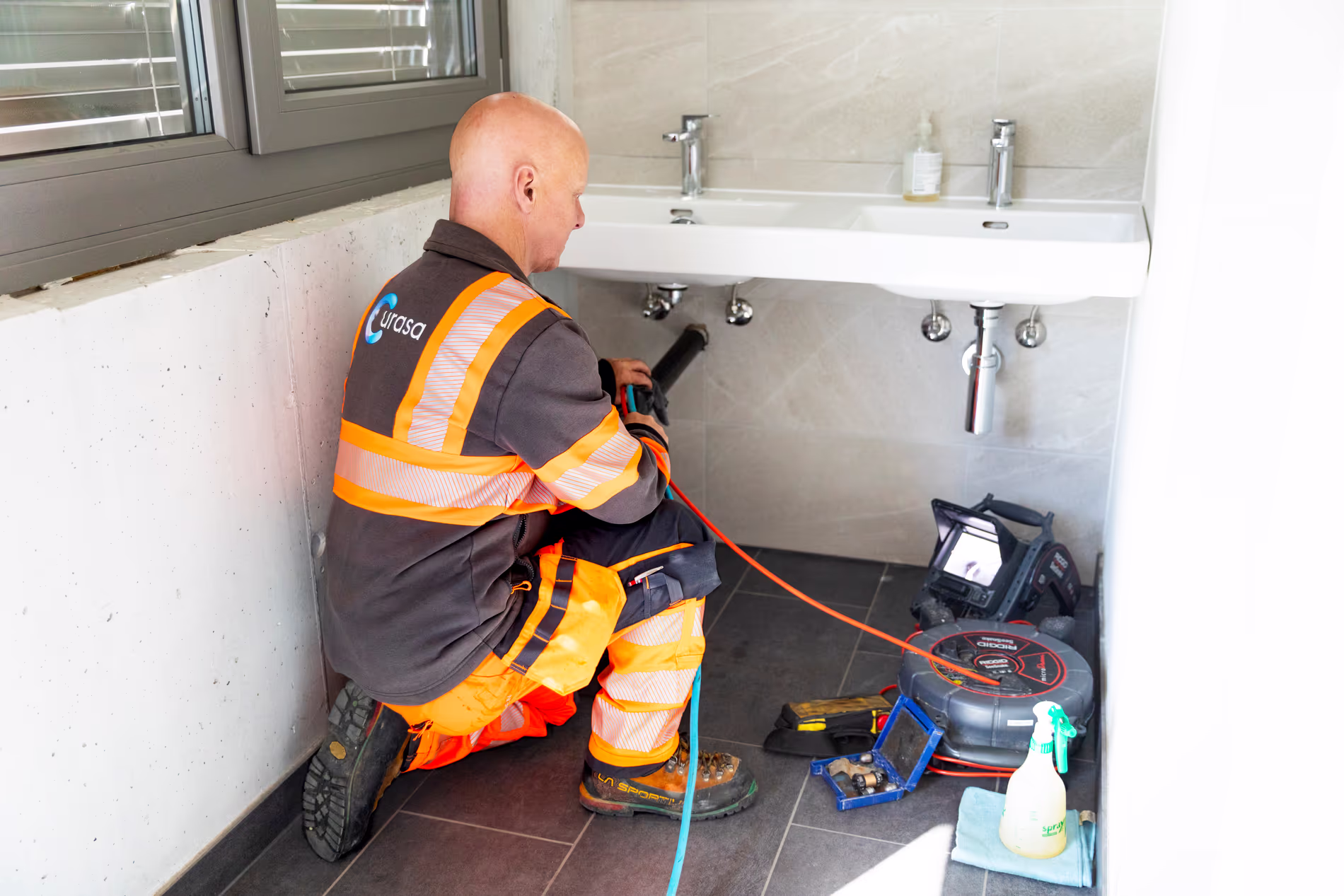 Un employé est en train d'inspecter les tuyaux d'un évier dans une salle de bain