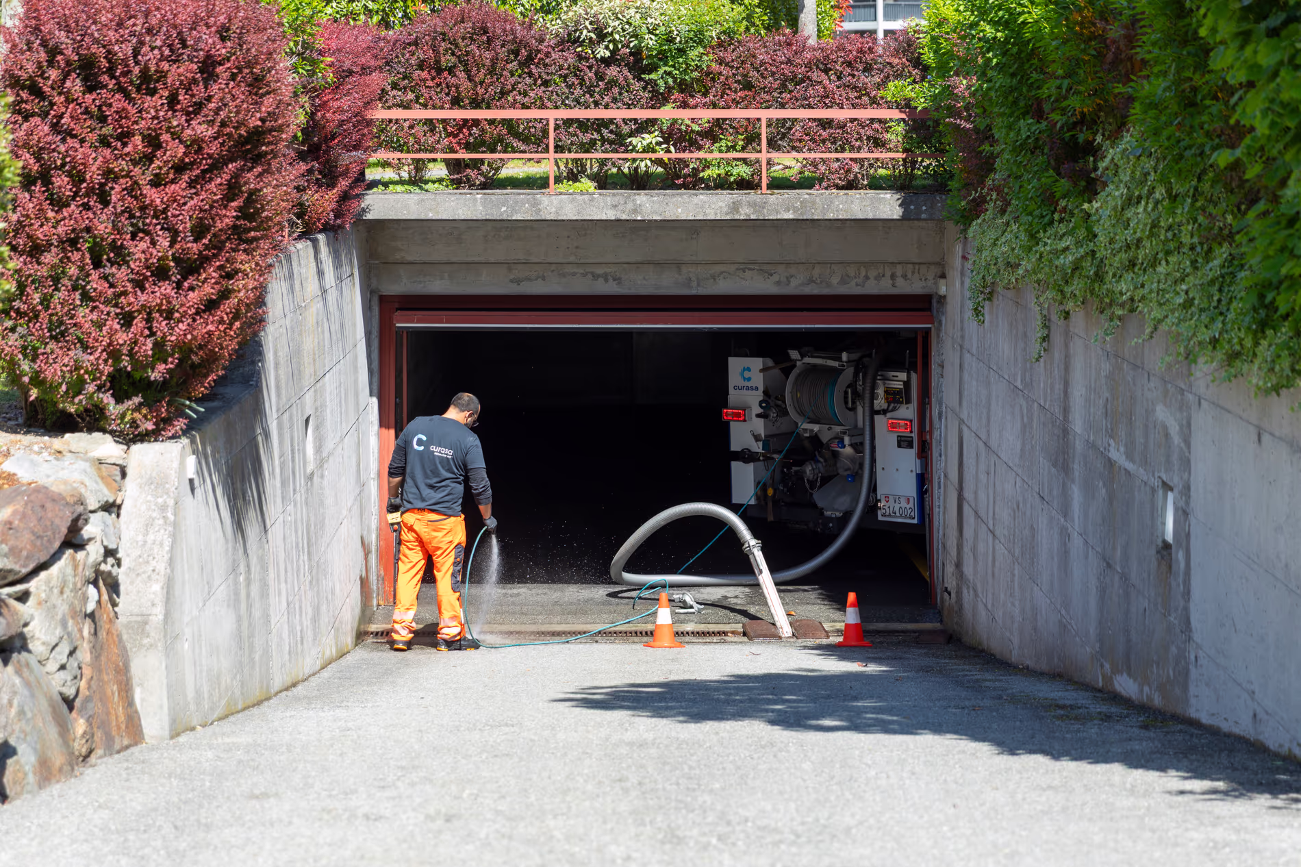 Un employé est en train de nettoyer au jet une rigole d'écoulement à l'entrée d'un parking
