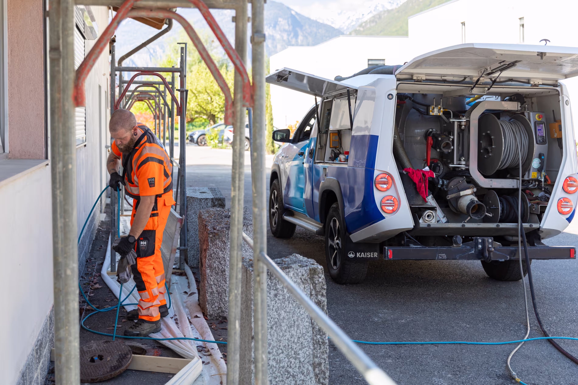 Un employé tire un cable depuis une bouche d'égout à côté d'un immeuble en chantier