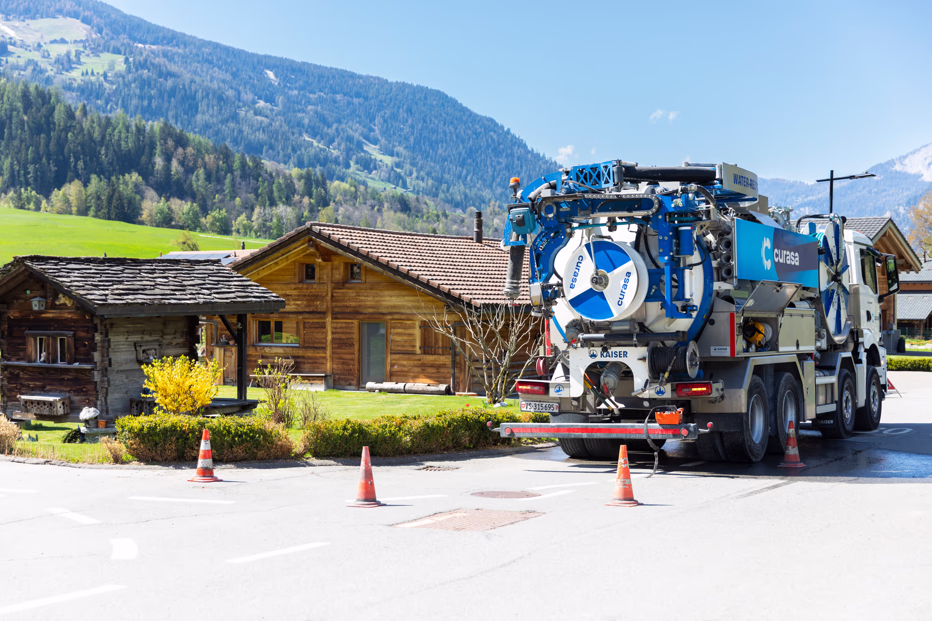 Un camion de recyclage d'eau est parké dans un village de montagne. Des cones sont posés autour du camion