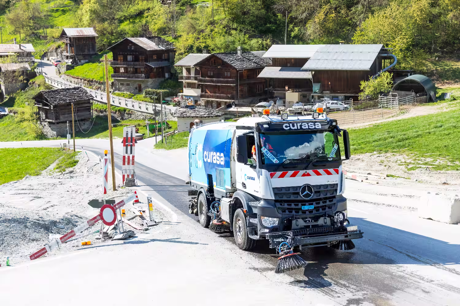 Un camion balayeuse de face sur une route dans un village d'alpage. Le camion nettoie la route poussiéreuse dû au chantier. 