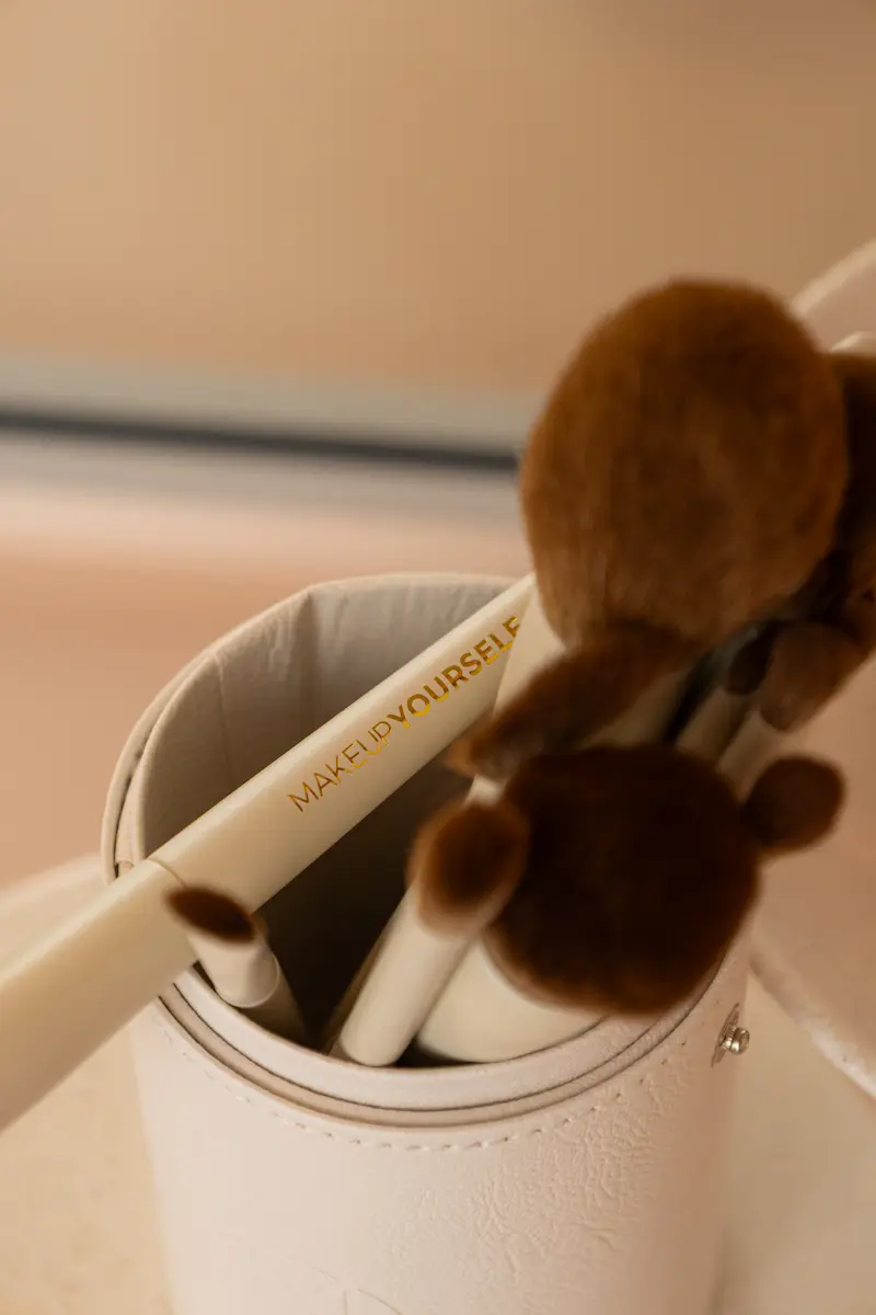 Various shades of pink and purple lipstick and blush swatches on a light pink background, including creamy, glossy, and powder textures.