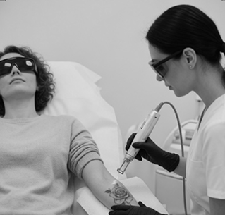Tattoo removal procedure on woman’s forearm by technician using laser device, both wearing protective glasses.