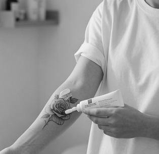 Person applying cream from a tube onto a tattoo of a rose on their forearm.