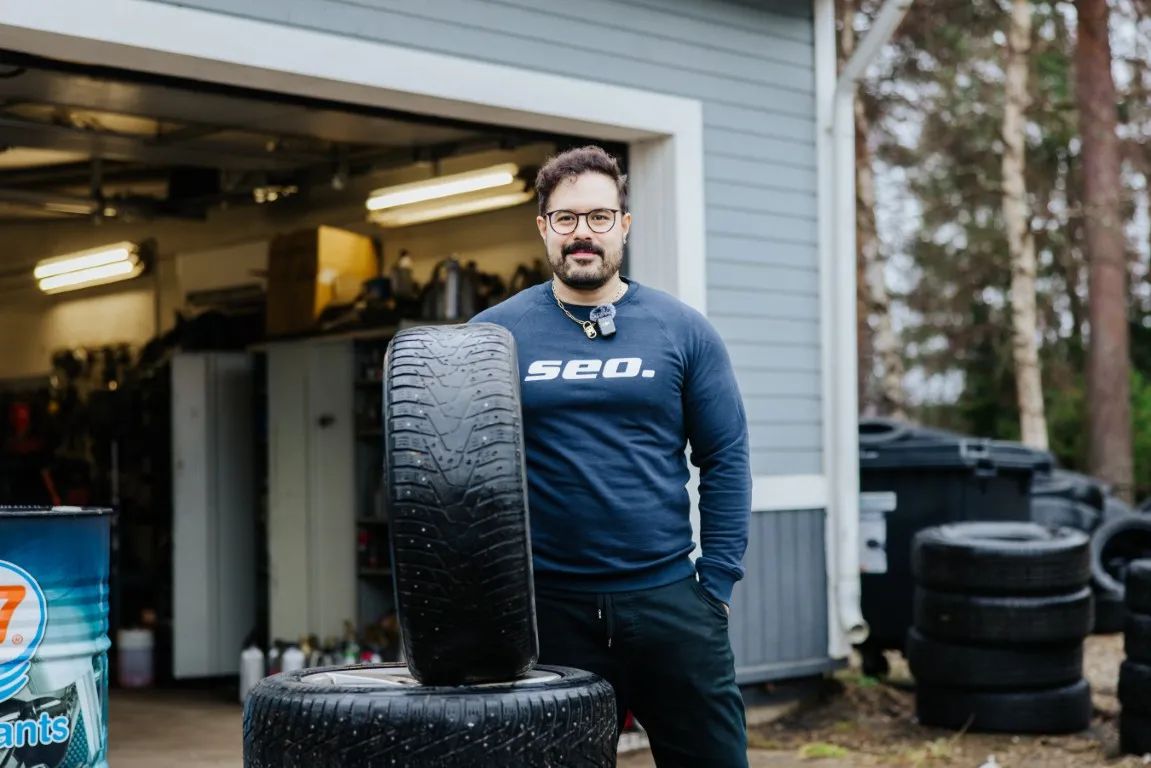 Mekaanikko seisoo korjaamon ovella autonrenkaiden kanssa