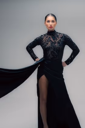 Woman in a sheer black dress with lace details and high slit posing with hands on hips.