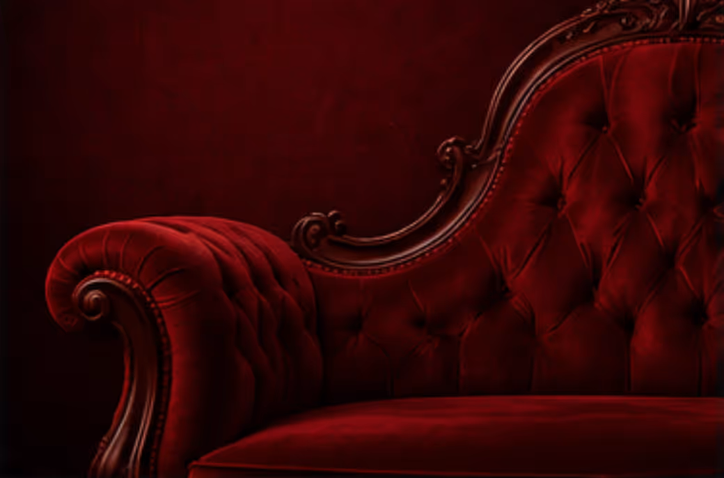 Close-up of a luxurious dark red velvet antique sofa with ornate wood carvings.