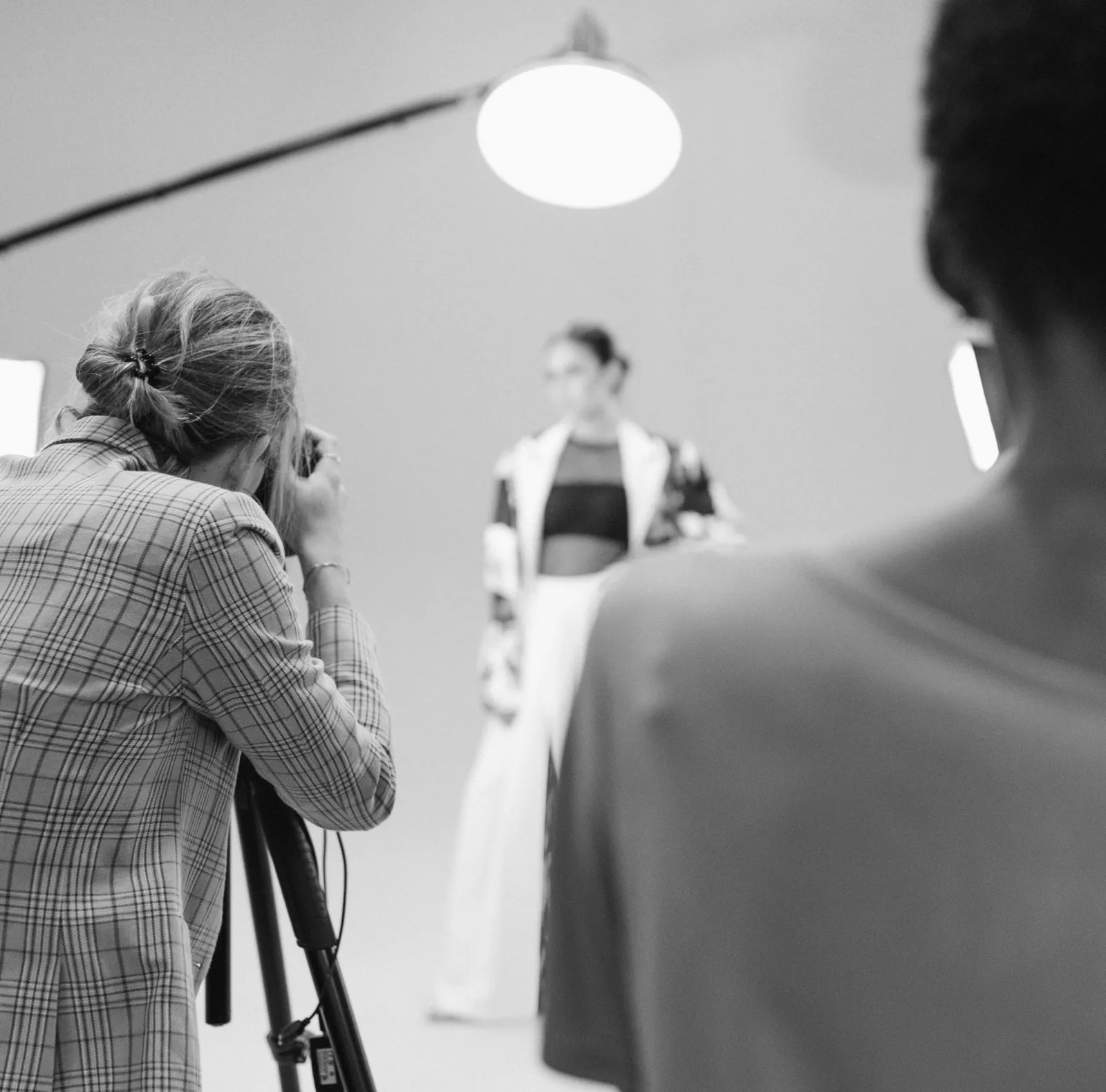 Photographer with a camera on a tripod taking a picture of a blurred model during a studio photoshoot with professional lighting equipment.