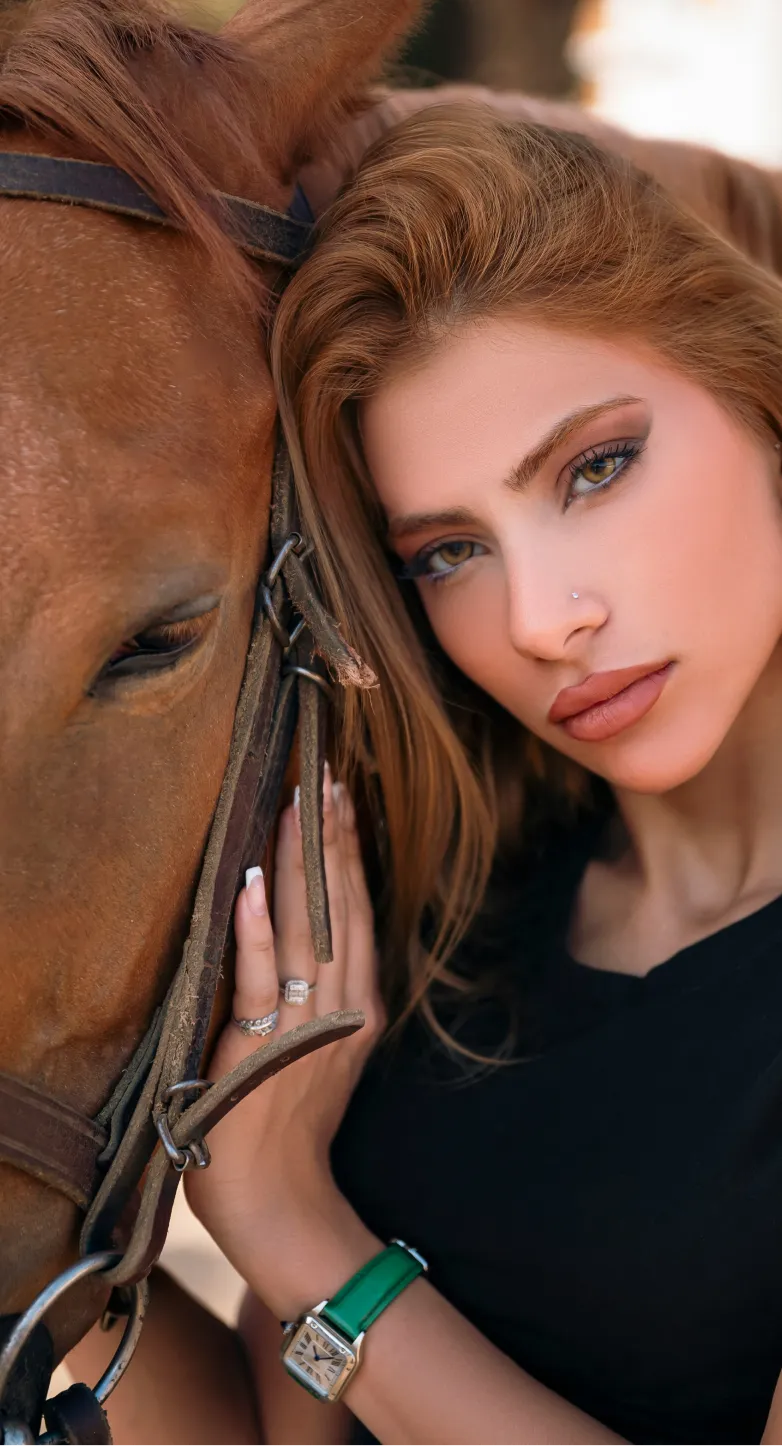Close-up of woman with red hair gently touching a brown horse beside her face.