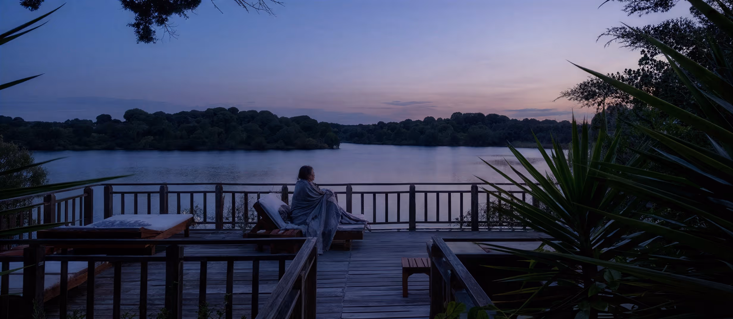 A guest on the timber deck at Hotel Vale do Gaio at dusk, looking out over the reservoir