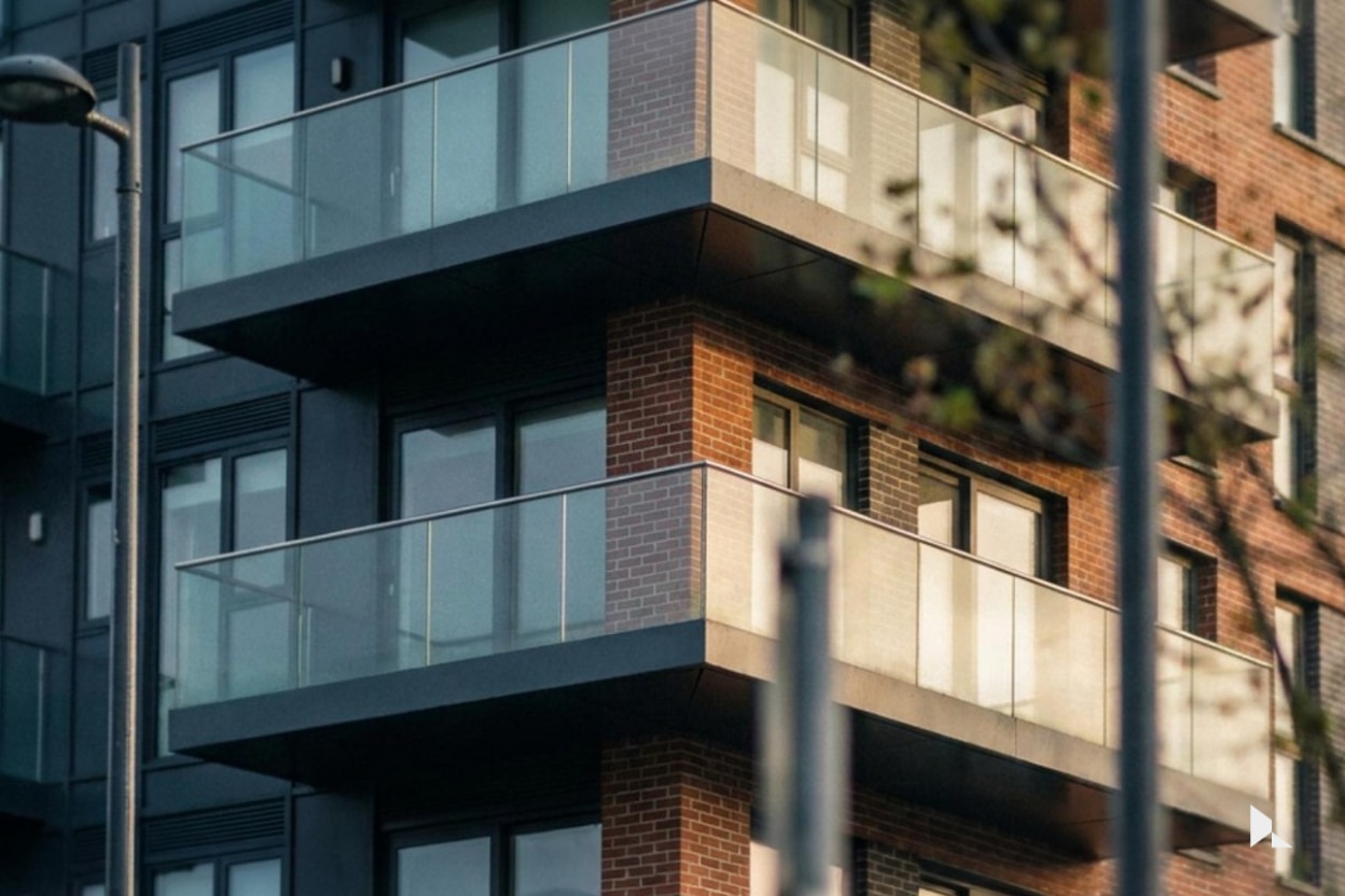 Glass balconies on a red-brick and dark-clad apartment building at Glass Bottle, Dublin, in low evening light