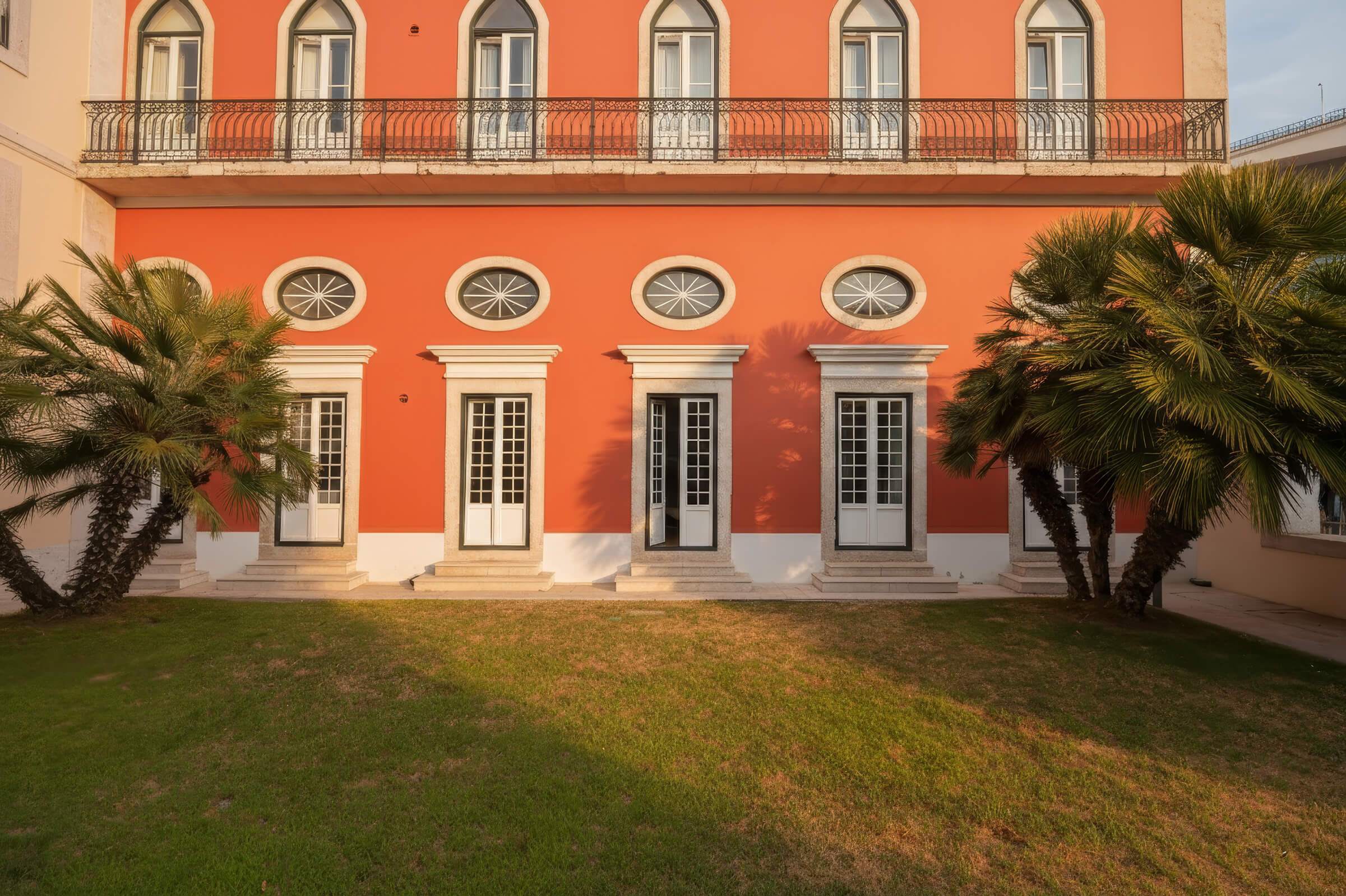 The coral façade of Palácio da Junqueira, with arched windows and palm trees on the lawn