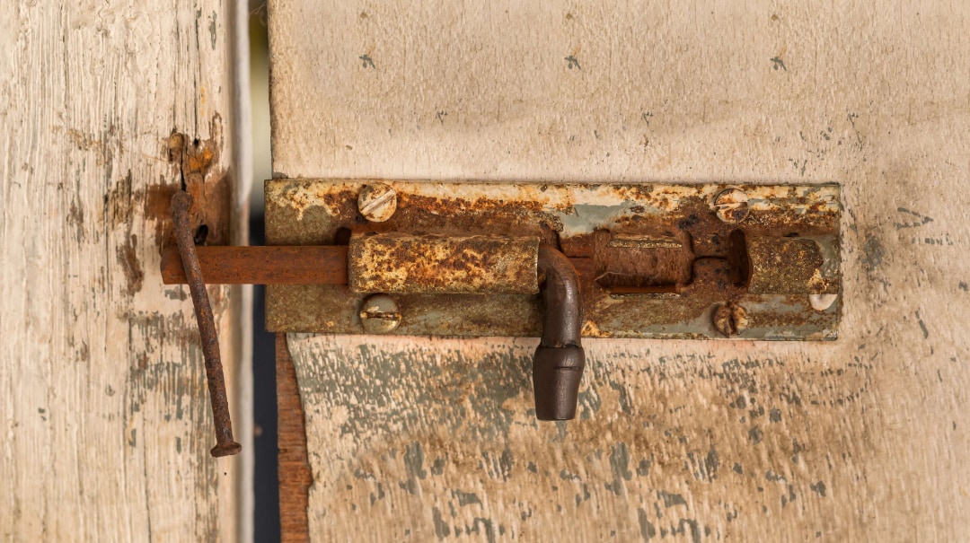 A rusted bolt holding a weathered painted door shut