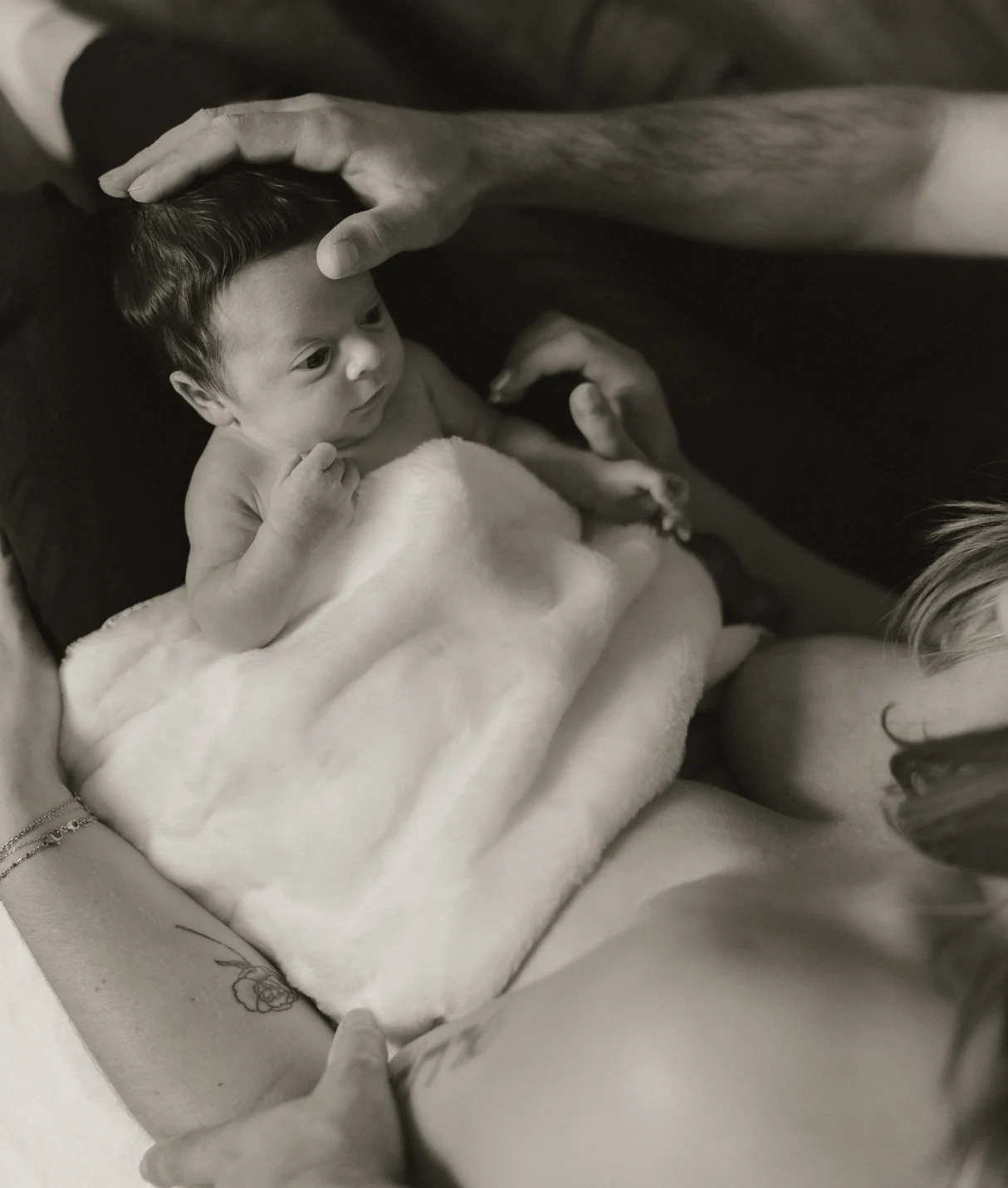 Nouveau né dans les bras de sa maman et de son papa qui lui caresse la tête