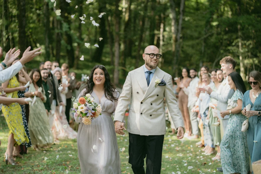 Jeune mariés marchant dans l'allée d'une foret, et les invités qui célèbrent leur mariage en jetant des pétales de fleurs 
