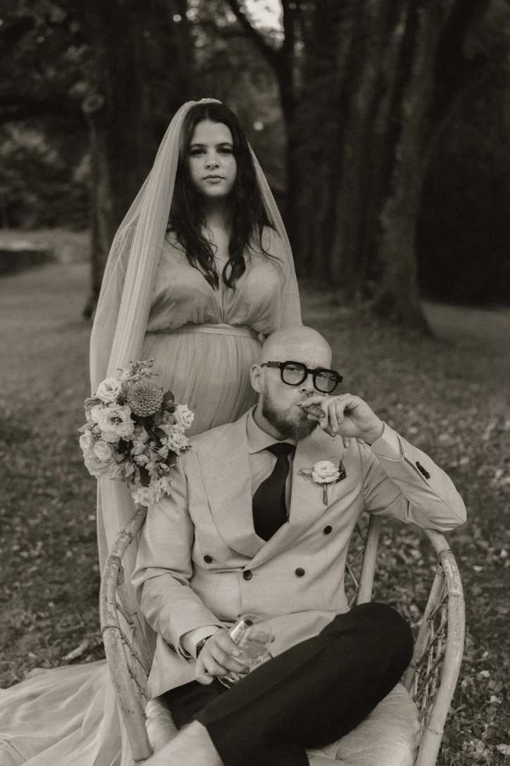 Couple de mariés dont le mari est assis tenant un cigare et la femme et derrière lui - image vintage