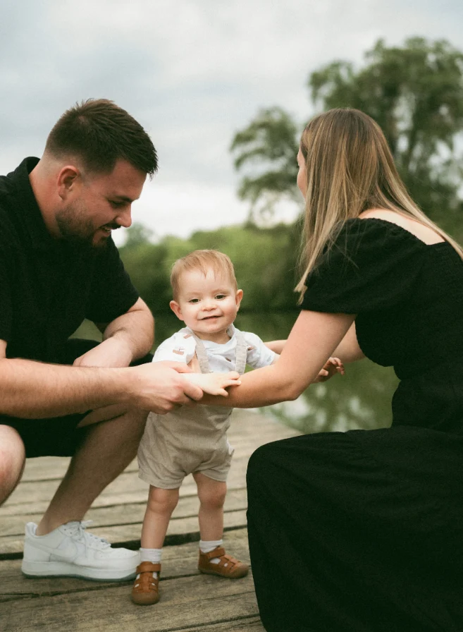 Parents accroupis accompagnant leur petit garçon à se tenir debout sur un ponton