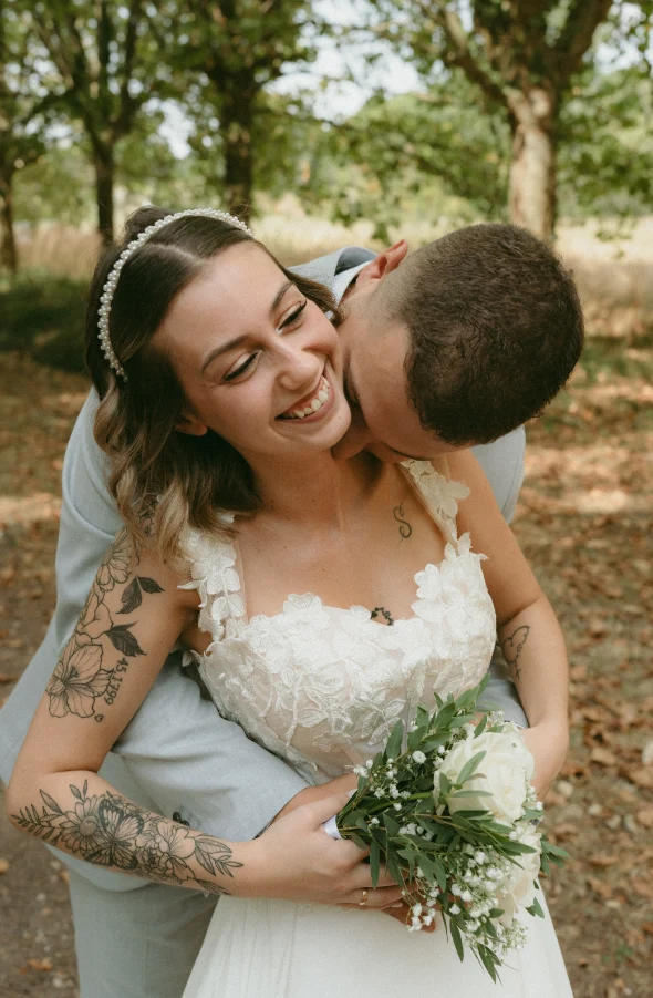 Couple de marié dont le mari fait un bisou dans le cou de sa femme