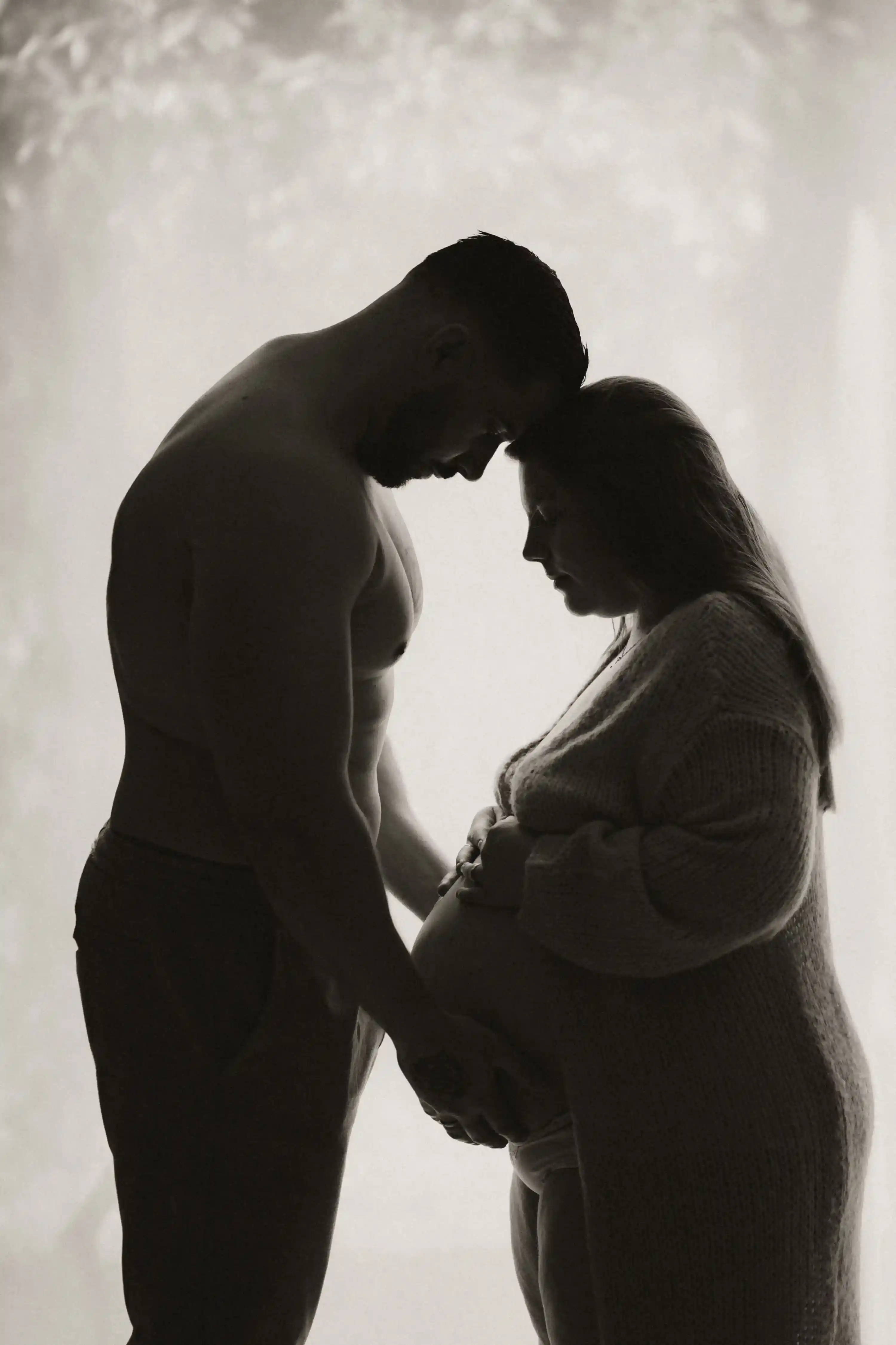 Portfolio maternité couple de futurs parents face à face caressant le ventre rond de la femme enceinte