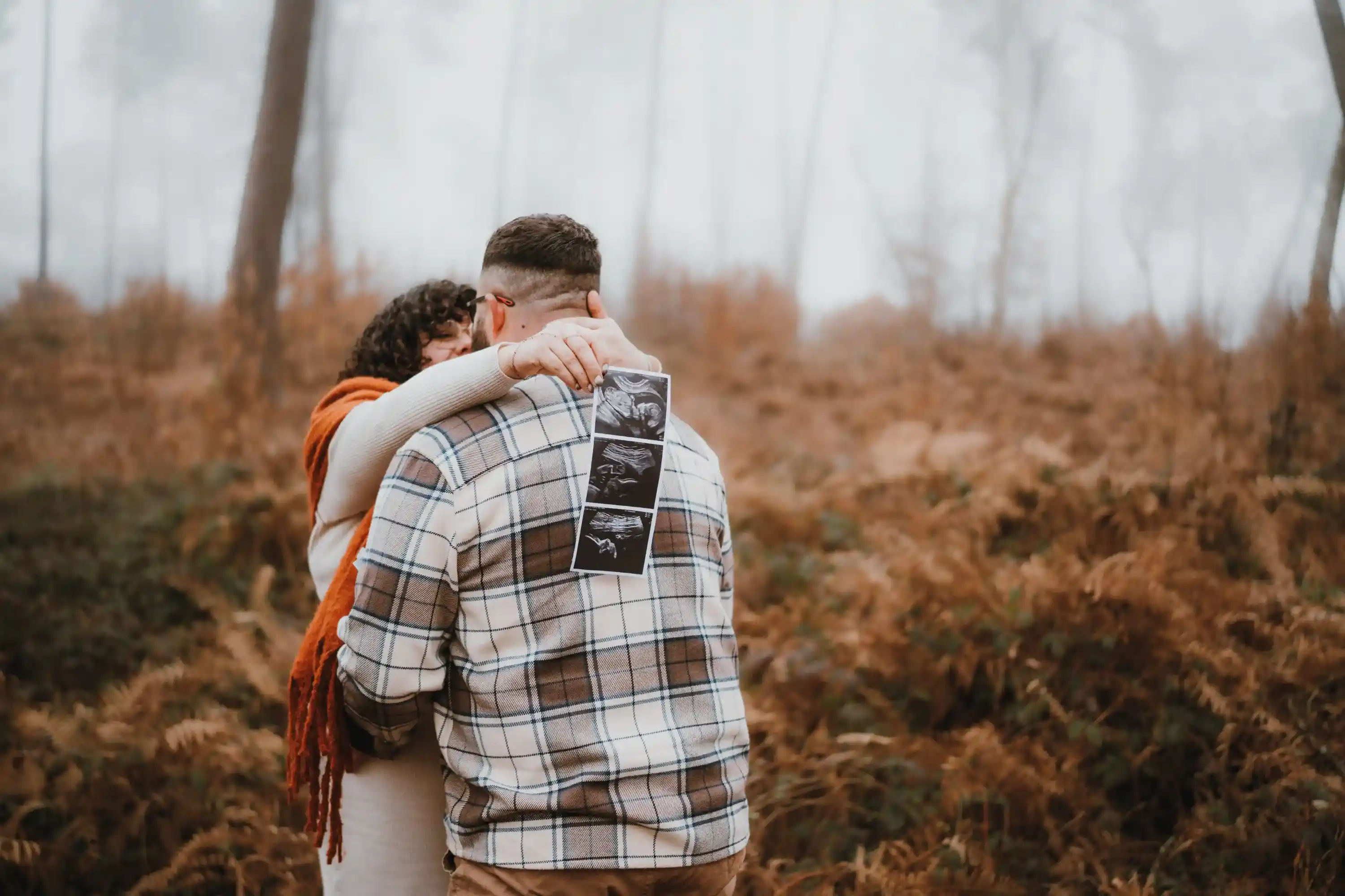 Couple enlacé annonçant une grossesse avec des échographies du bébé dans la foret 