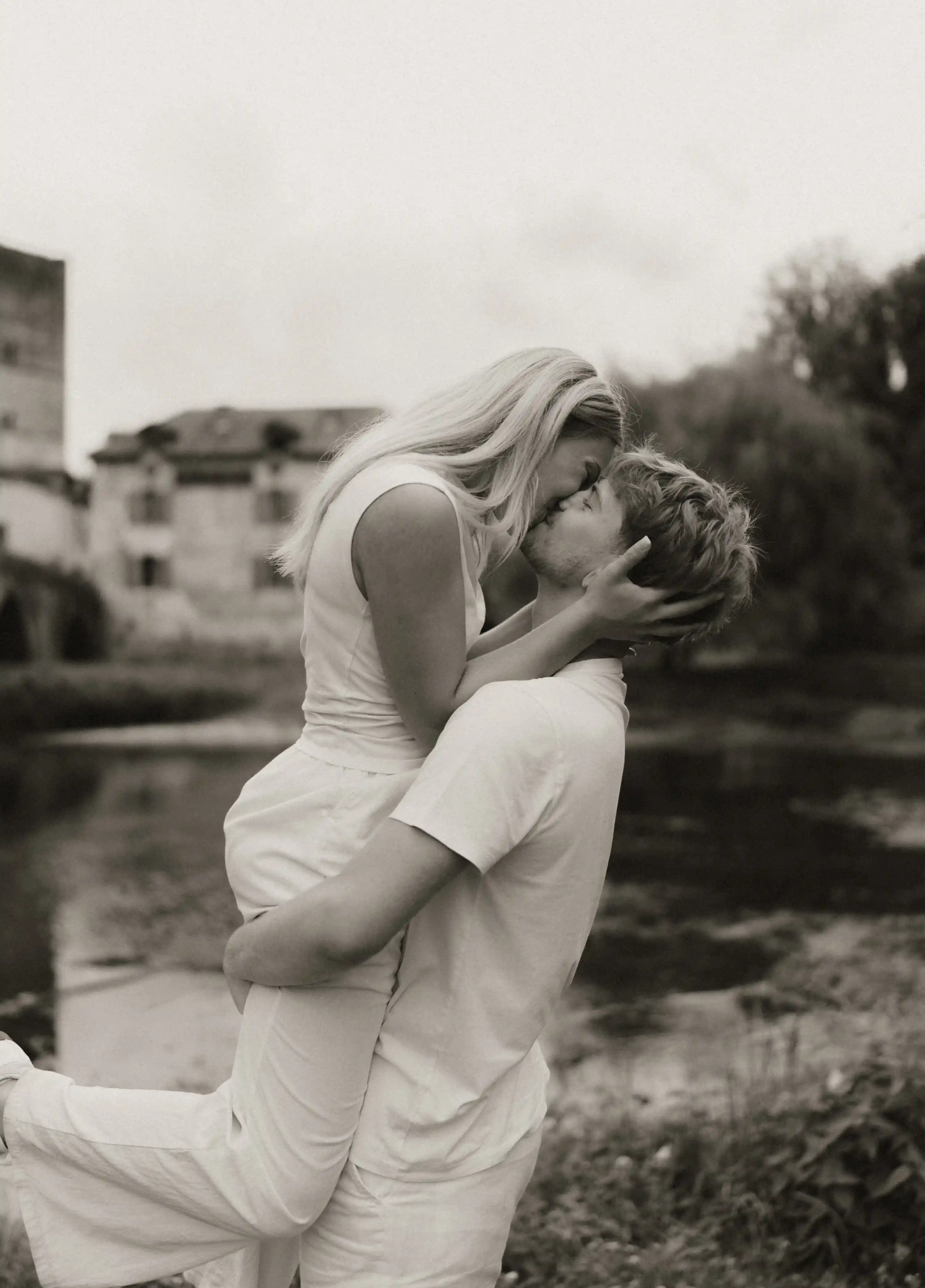 couple amoureux s'embrassant au bord d'un lac et l'homme porte la femme 