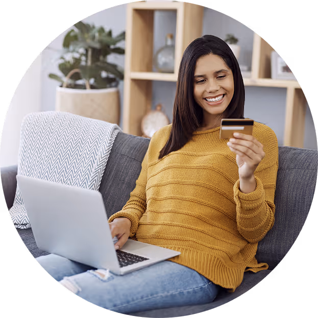 Smiling woman sitting on a gray couch using a laptop and holding a credit card.