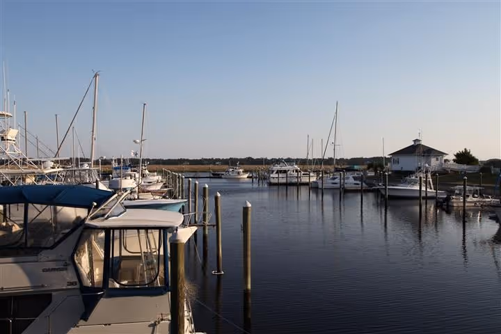 Calm marina with boats docked along piers under a clear sky at sunset.