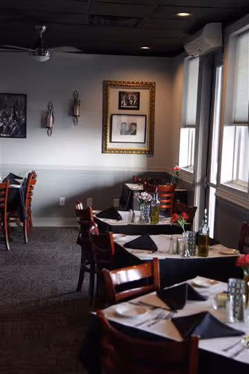 Cozy restaurant interior with wooden chairs, tables set with black napkins, flowers, and framed black-and-white photos on the walls.