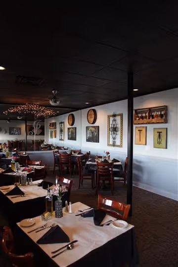 Interior of a cozy restaurant with dark wood chairs, tables set with white and black linens, and decorative artwork on white walls.