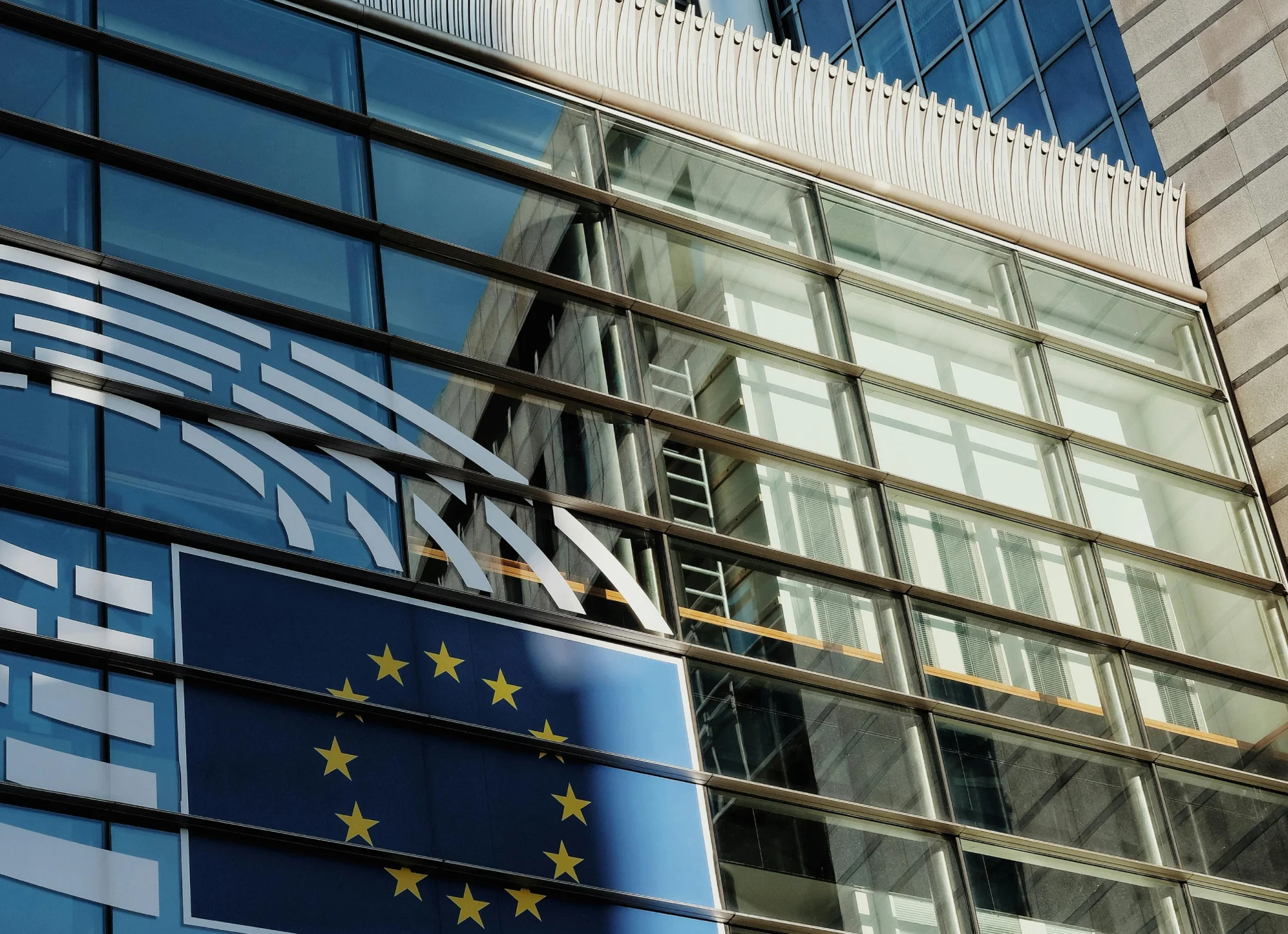 Reflection of a building and the European Union flag on a glass facade with metal framing.