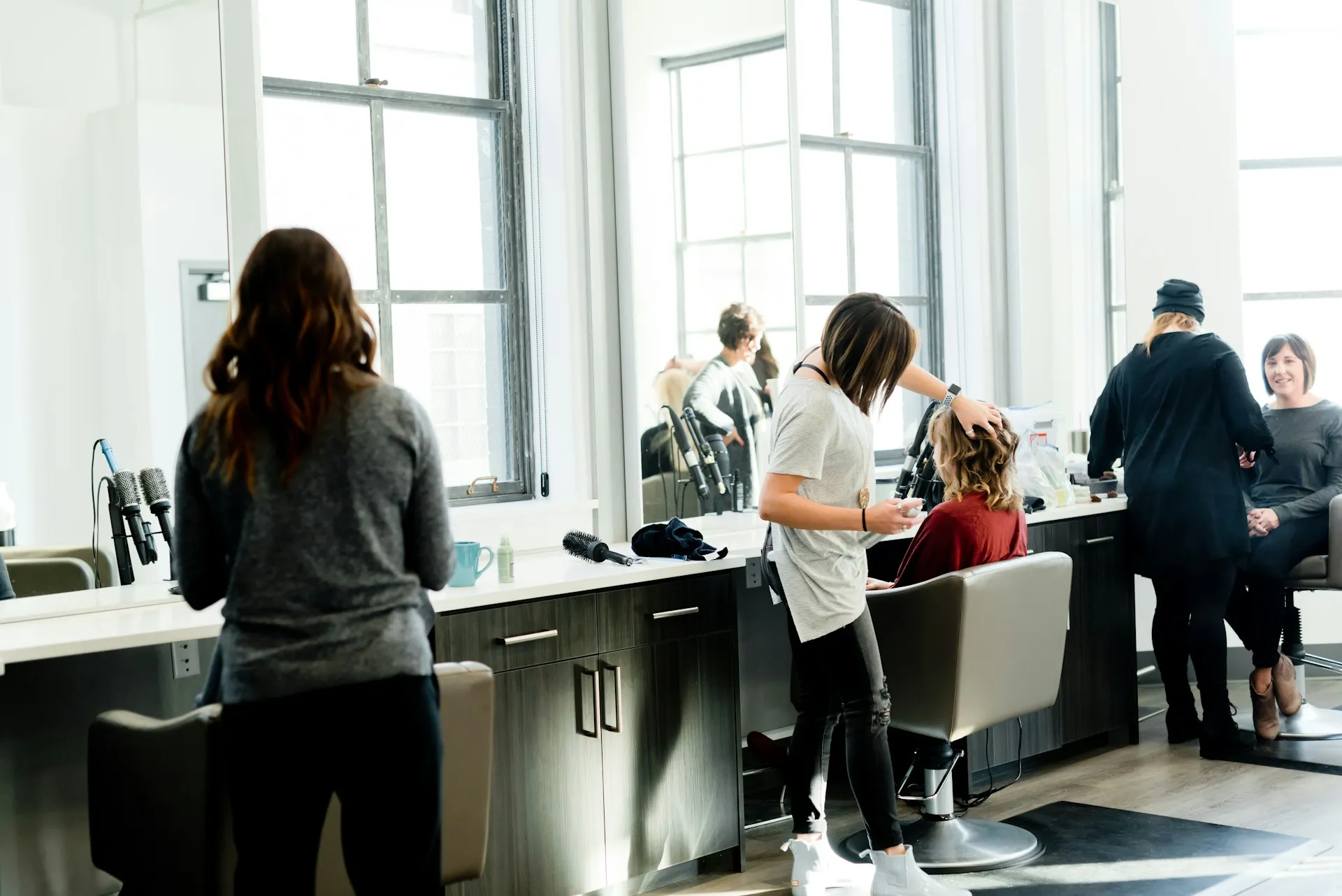 Hair salon with two stylists working on clients seated in chairs in front of large mirrors and windows.