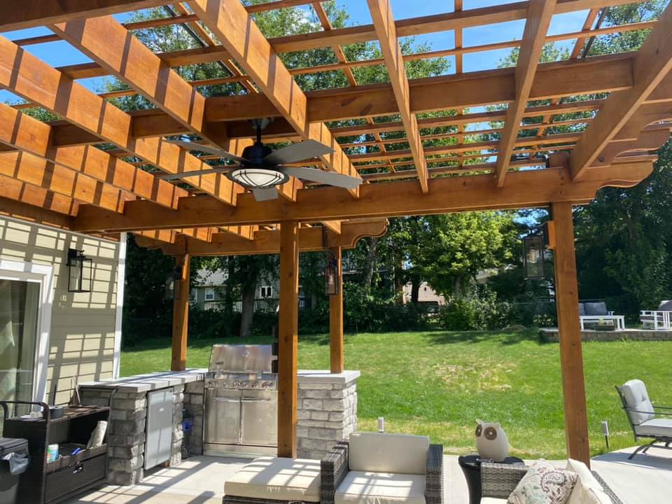 Backyard patio with a wooden pergola, ceiling fan, and built-in outdoor kitchen.