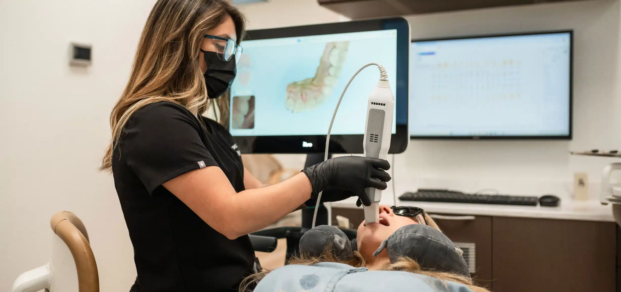 Dental professional wearing gloves and a mask using an intraoral scanner on a patient reclining in a dental chair.