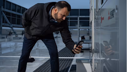 Man in black jacket inspecting equipment outdoors using a handheld device at dusk.