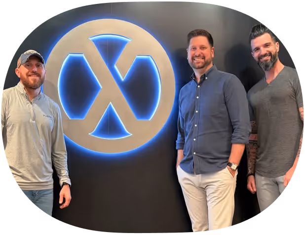 Three men standing and smiling by a black wall with a large glowing circular logo.