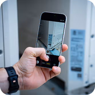 Hand holding a phone capturing a close-up photo of equipment with labels and QR code.