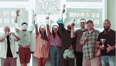 Nine people standing in a row holding trophies and smiling in front of a presentation screen.