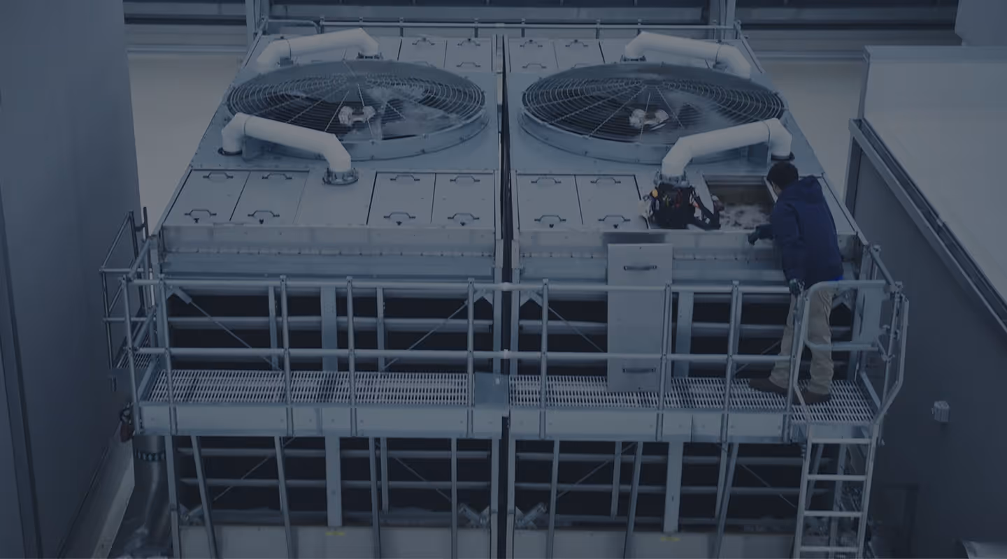 Technician inspecting and repairing large industrial HVAC cooling units on building rooftop.