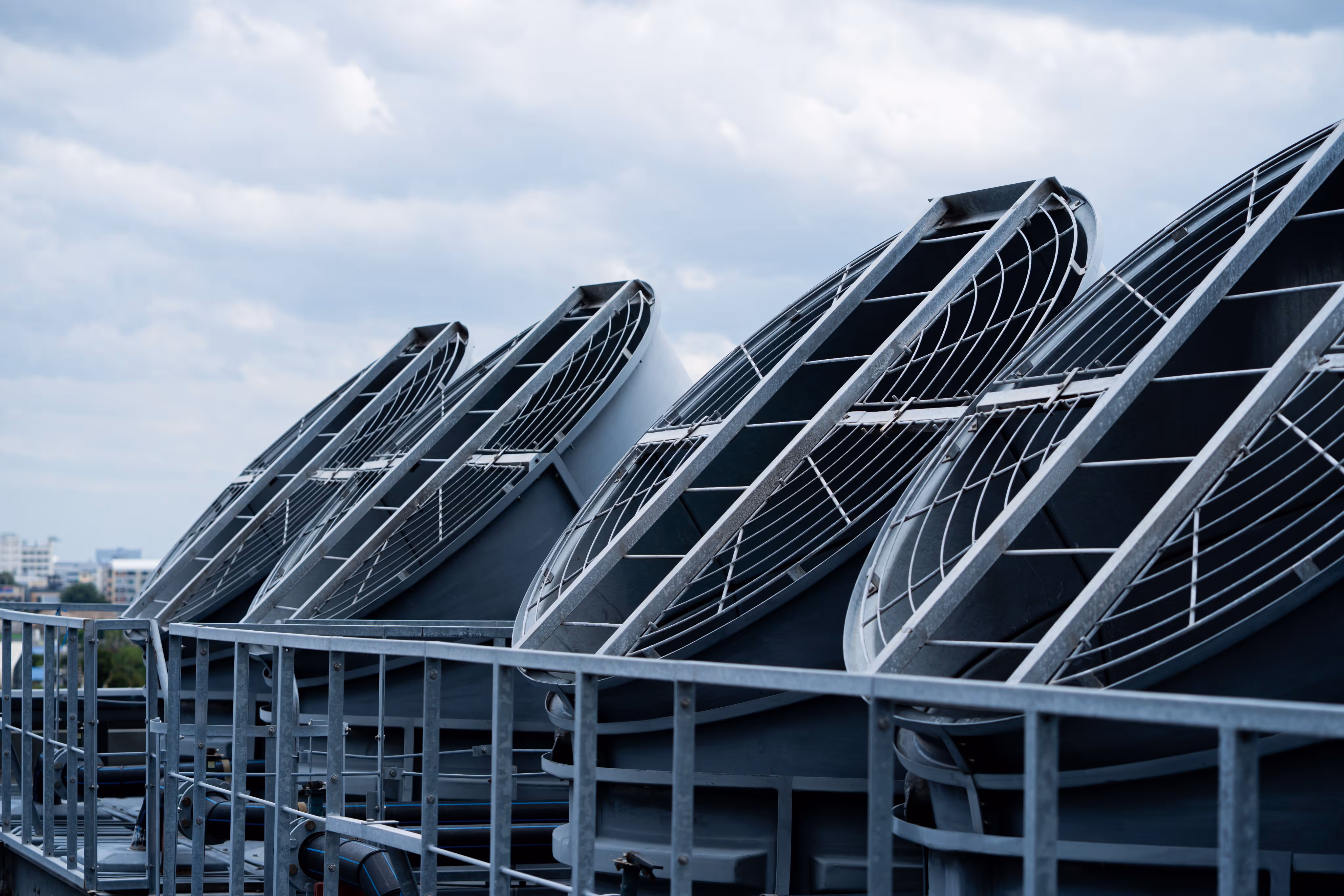Row of large industrial exhaust fans with protective metal grills on a rooftop.